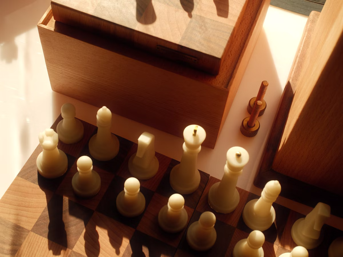 Photo of chess pieces on a wooden board with dramatic shadows.